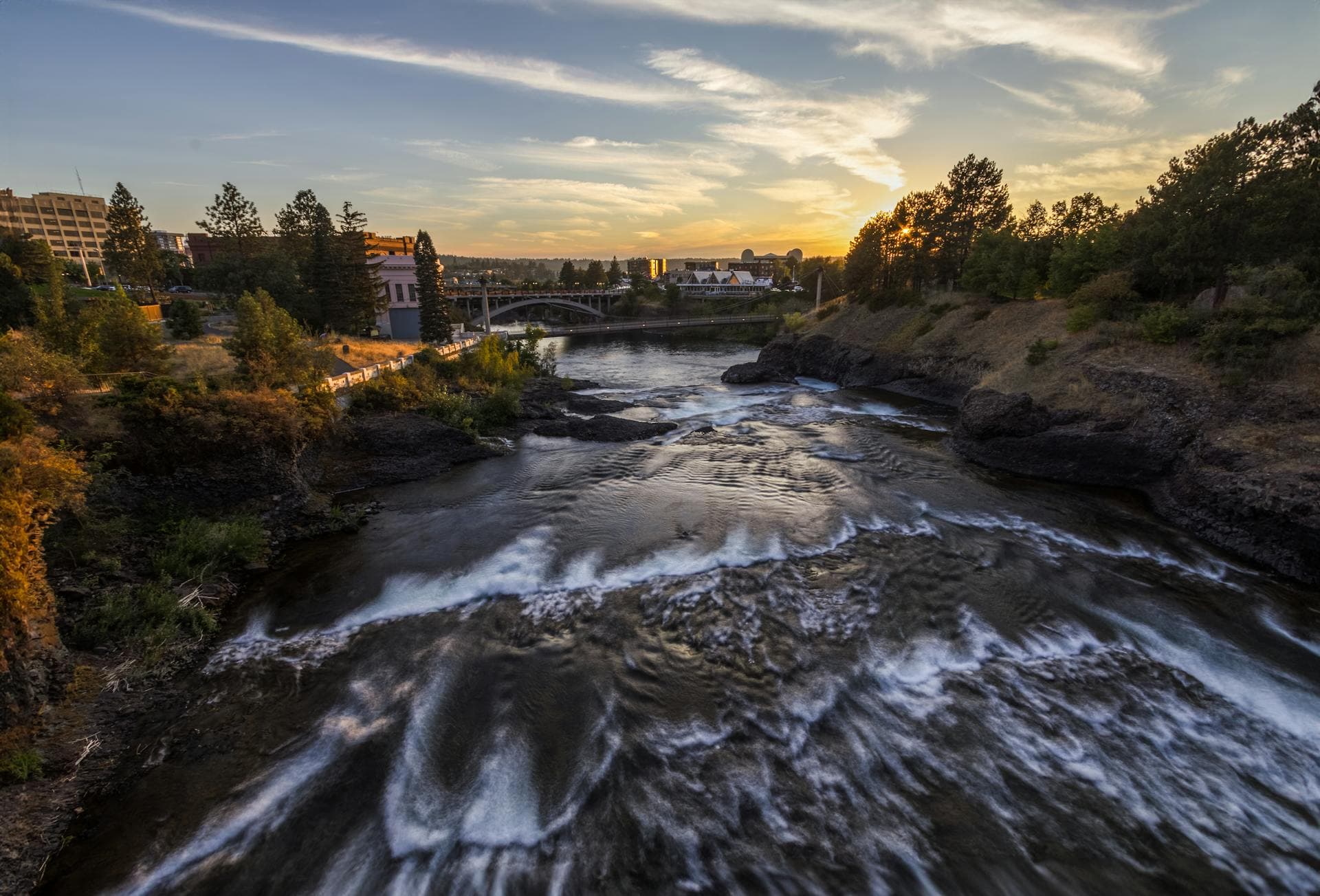 Spokane River flowing through city at sunset with urban landscape and pine trees